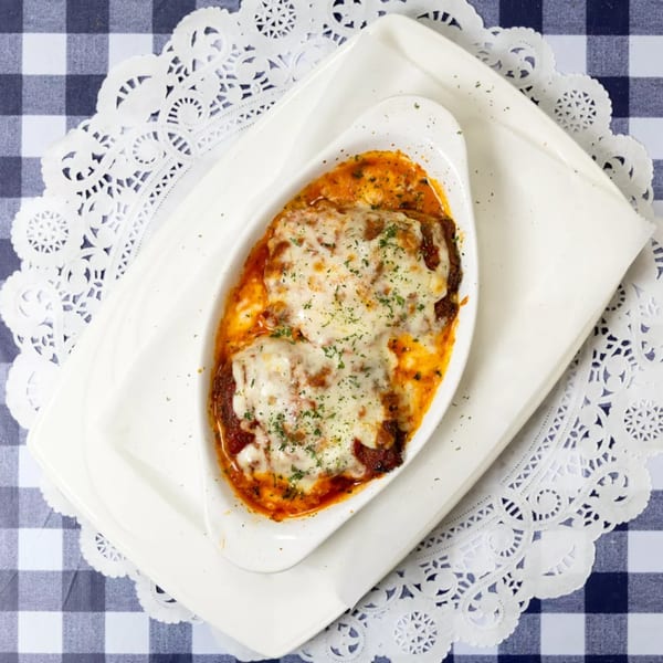 Baked lasagna with melted cheese and herbs in a white dish on a blue and white checkered tablecloth.