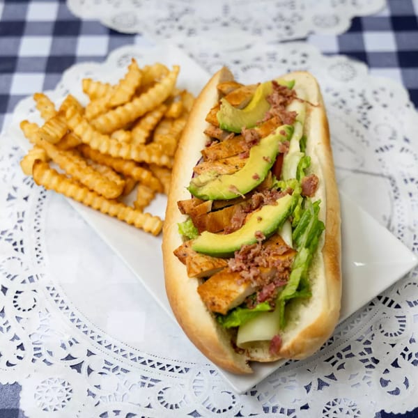 Chicken and avocado sub sandwich with bacon bits and crinkle-cut fries on a white plate.