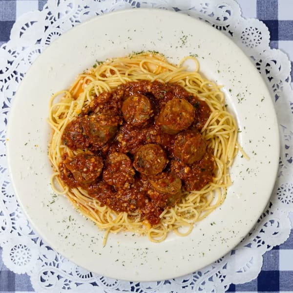 Spaghetti with meatballs and rich red sauce, garnished with herbs, on a white plate.