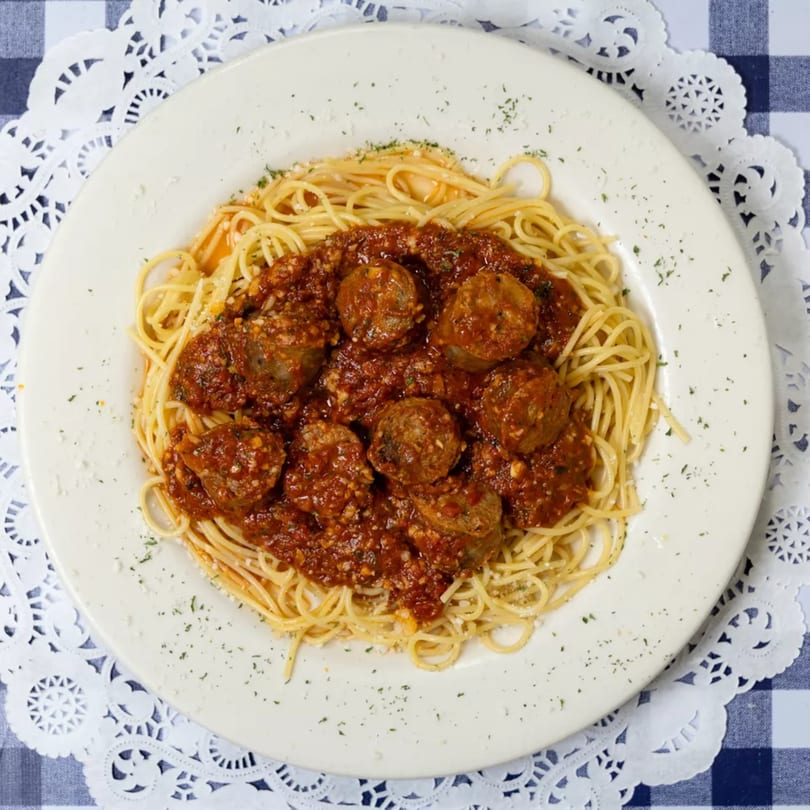 Spaghetti with meatballs and rich red sauce, garnished with herbs, on a white plate.