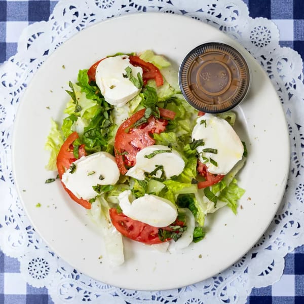 Fresh Caprese salad with mozzarella, tomatoes, basil, and lettuce, with a side of dressing.