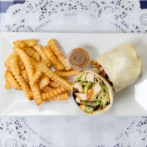 Chicken Caesar wrap with crinkle-cut fries and a side of dressing on a white plate.