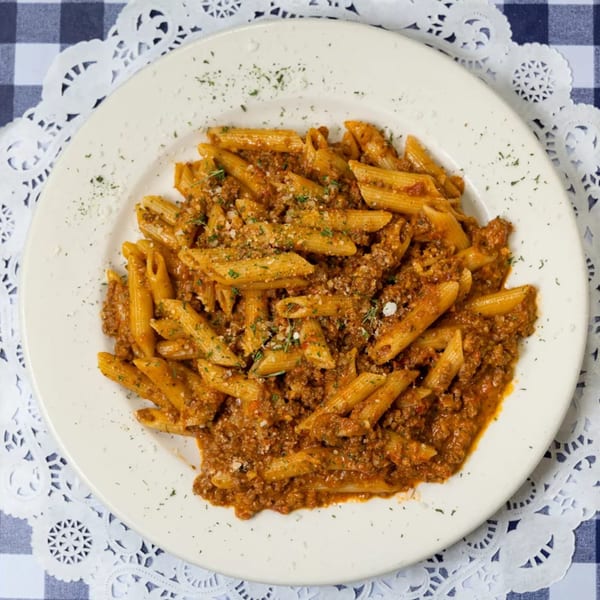 Penne pasta with rich bolognese sauce, sprinkled with parmesan cheese and herbs on a white plate.