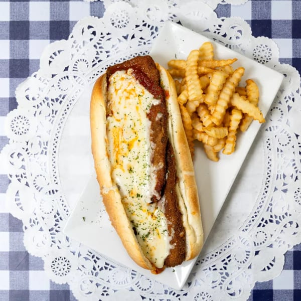 Chicken parmesan sub with melted cheese and sauce, served with crinkle-cut fries on a white plate.