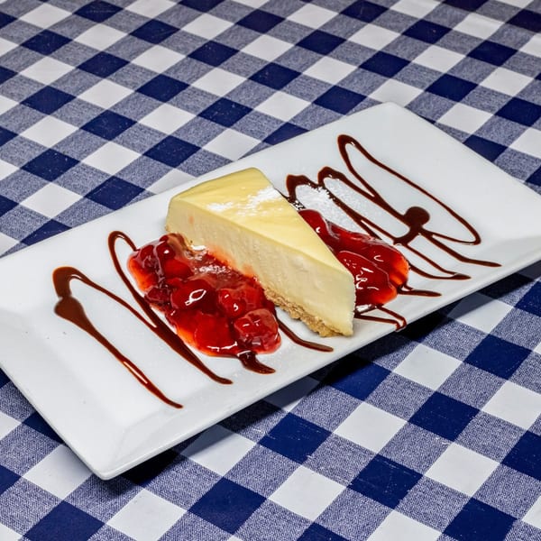 A slice of cheesecake with strawberry topping and chocolate drizzle on a white plate.