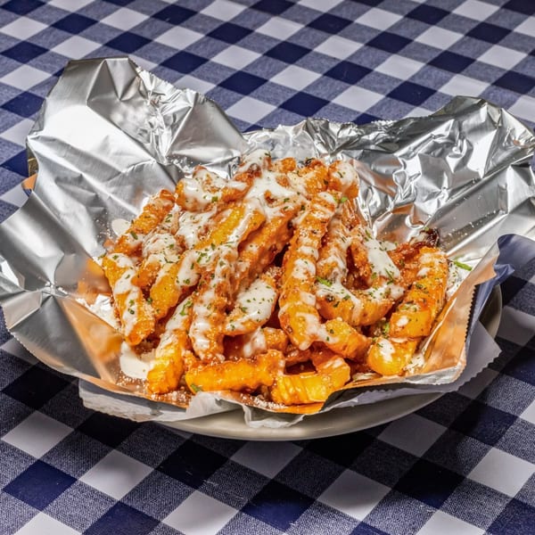 Waffle fries topped with white sauce, Parmesan cheese, and parsley in a foil-lined basket.