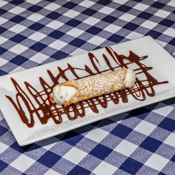 A cannoli dusted with powdered sugar and drizzled with chocolate sauce on a white plate.