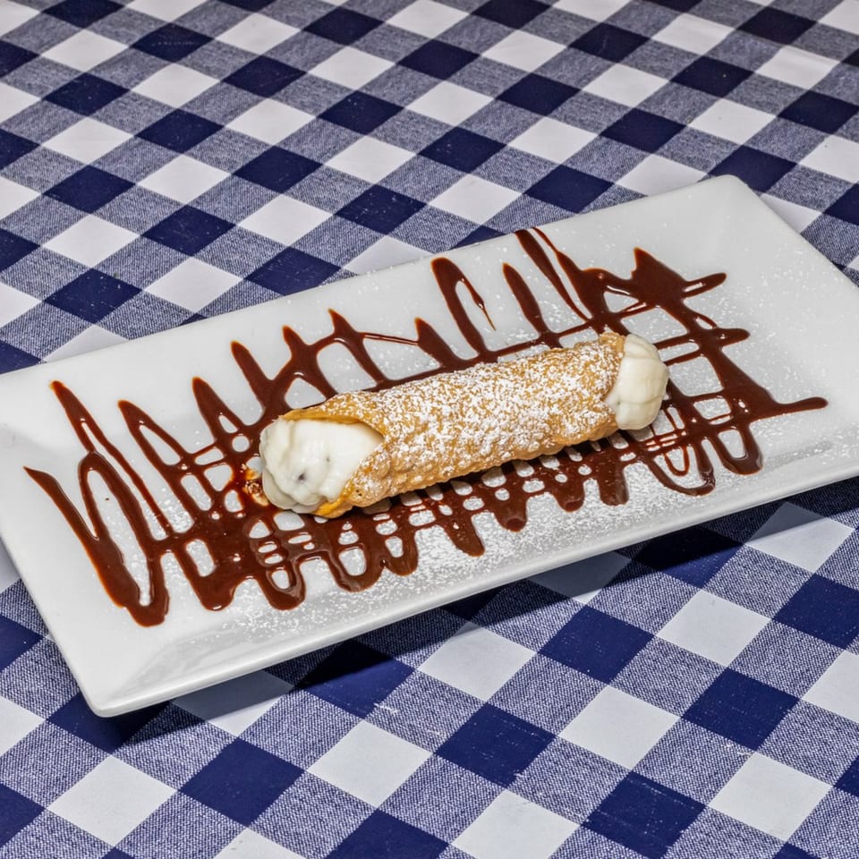 A cannoli dusted with powdered sugar and drizzled with chocolate sauce on a white plate.