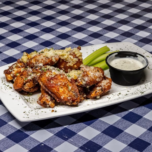 A plate of crispy chicken wings topped with parmesan cheese, served with celery sticks and ranch dressing.