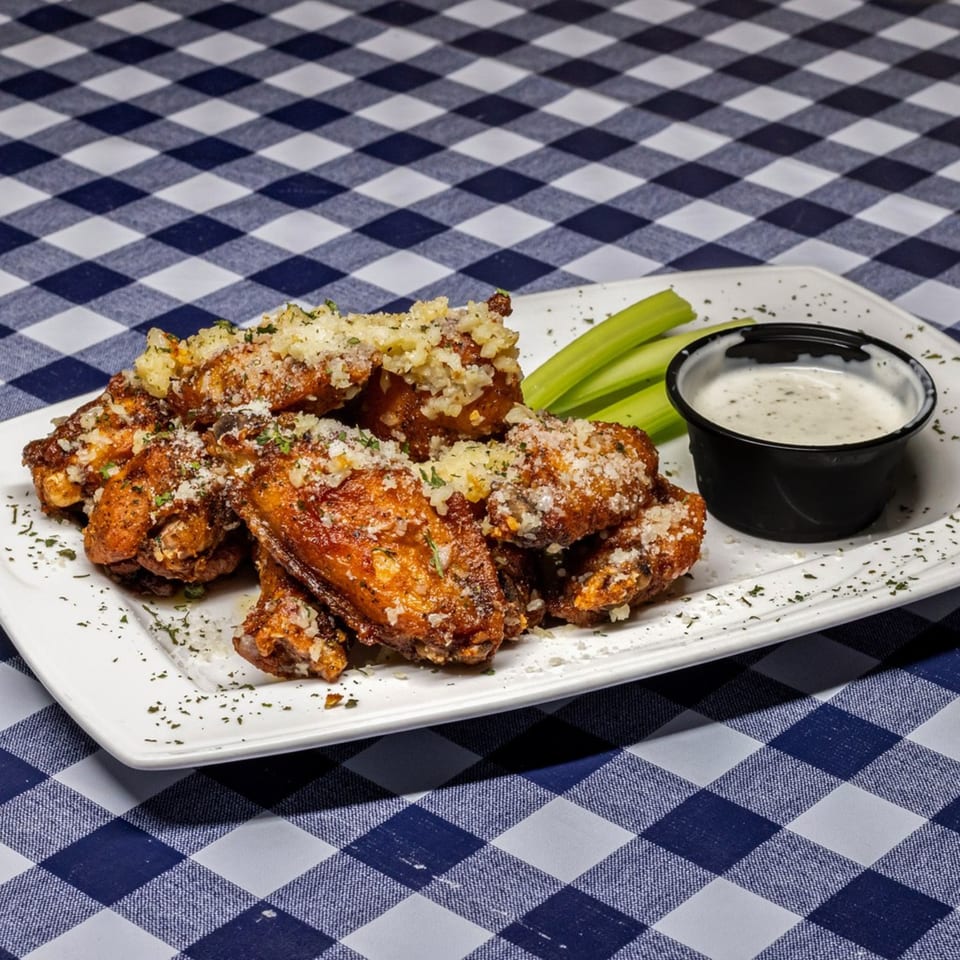 A plate of crispy chicken wings topped with parmesan cheese, served with celery sticks and ranch dressing.