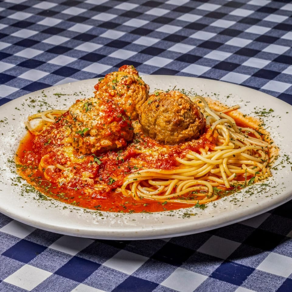 Spaghetti with three large meatballs, marinara sauce, and parsley on a white plate.