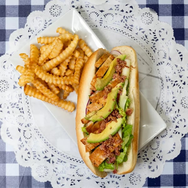 Chicken avocado sandwich with bacon bits and lettuce, served with crinkle-cut fries on a white plate.