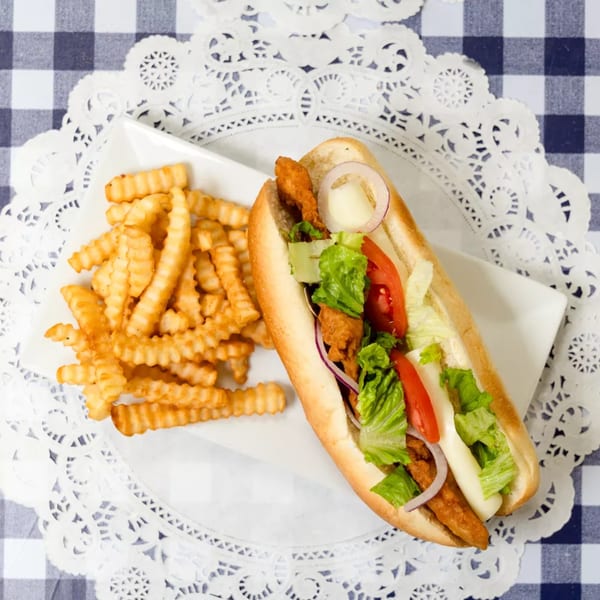 A fried chicken sandwich with lettuce, tomato, onion, and mayonnaise, served with crinkle-cut fries.