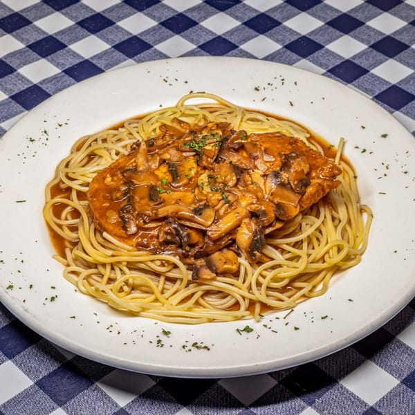 Chicken Marsala with mushrooms and spaghetti on a white plate, on a blue and white checkered tablecloth.