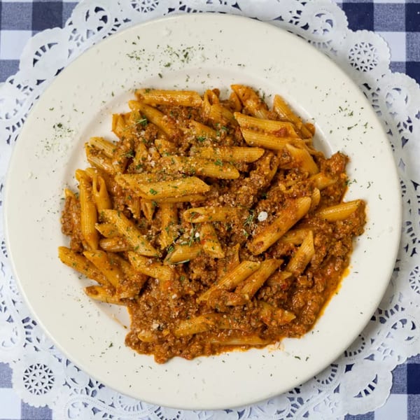 Penne pasta with a rich meat sauce, sprinkled with cheese and herbs, on a white plate.