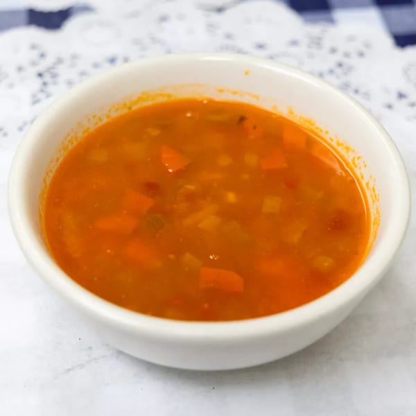A white bowl filled with a vibrant orange vegetable soup, featuring diced carrots and other vegetables.