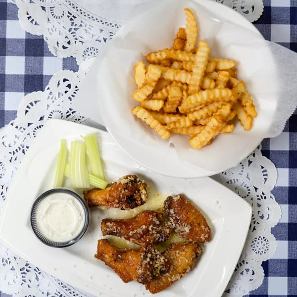 Garlic Parmesan wings with celery, ranch, and crinkle-cut fries on a blue and white checkered tablecloth.